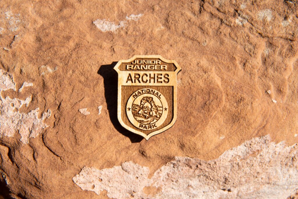 Arches Junior Ranger badge made o wood against a rock backdrop.